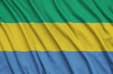 Gabon flag is depicted on a sports cloth fabric with many folds. Sport team waving banner