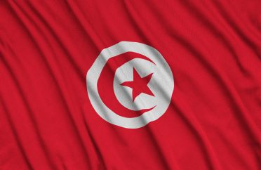 Tunisia flag is depicted on a sports cloth fabric with many folds. Sport team waving banner