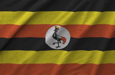 Uganda flag depicted on folded wavy fabric of old cloth